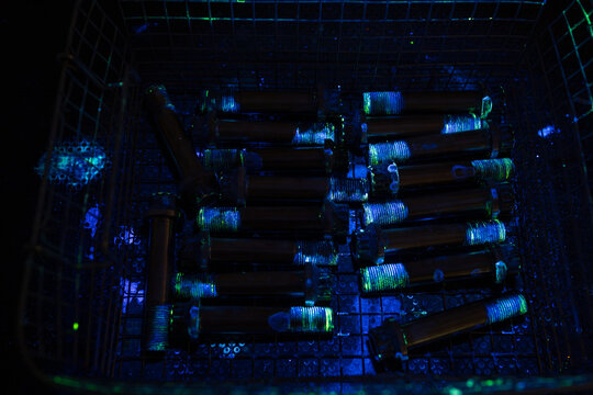 Metal bolts undergoing fluorescent penetrant inspection FPI under ultraviolet light, showing defect detection for non-destructive testing and manufacturing quality control