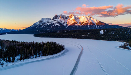 Snowy mountain landscape at sunrise frozen lake and forest.