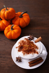 Vertical picture of tasty pumpkin spice latte with whipped cream in cup, anise and cinnamon on wooden table.
