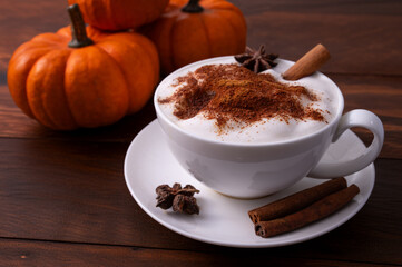 Pumpkin Spice Latte pumpkin drink topped with whipped cream sits in a white cup. Surrounding it pumpkins and cinnamon sticks creating a festive fall atmosphere.