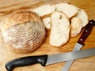 Freshly Baked Round Artisan Bread Loaf with Sliced Pieces and Knife on Wooden Table