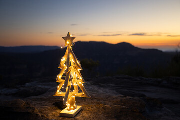 Christmas tree lit with fairy lights with a mountain backdrop and a sunrise or sunset sky.  Christmas in Blue mountains