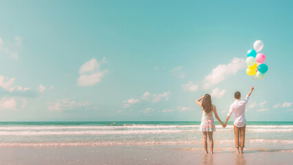 Portrait of couple of young happy married hipsters in trendy vintage clothes standing together on the beach with balloons. Sunny summer day. Pastel colors tone