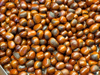 A top-down, full frame view of a large pile of glossy, brown roasted chestnuts filling the entire frame.
