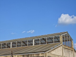 An old industrial building or warehouse with a skylight roof and concrete block walls, set against a clear blue sky with wispy clouds.