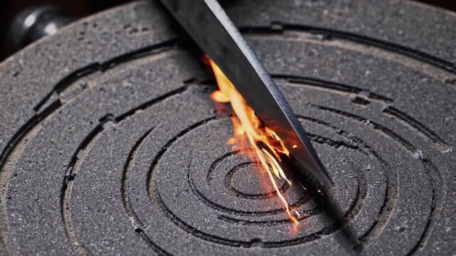 knife being sharpened on a grinding wheel, creating a shower of bright sparks, in a dark workshop environment