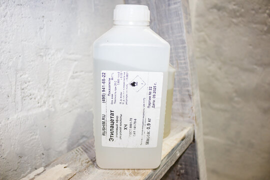 A white plastic chemical container labeled in Russian with ethyl acetate information rests on a weathered wooden shelf against a textured light background: Russia - November 18, 2025