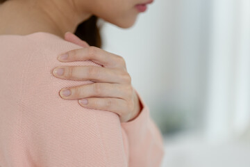 Close-up of Asian woman hand touching her shoulder, indicating pain or discomfort. Ideal for concepts of muscle tension, physical therapy, shoulder injury, stress or body ache.