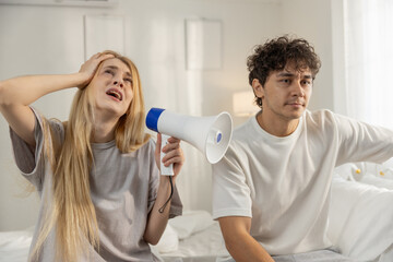 Angry women shouting with megaphone while man sits quietly, showing communication breakdown, couple conflict and relationship stress. Great for emotional arguments and marriage