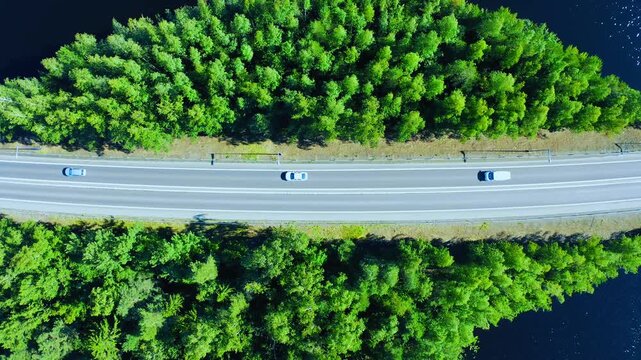 Aerial View of Cars Driving Along a Curved Road Surrounded by Lush Green Forests and a Scenic Water Body, Capturing Nature and Transportation Harmoniously