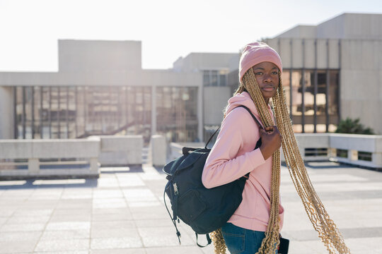 African American woman standing on rooftop plaza in pink hoodie carrying black backpack, copy space