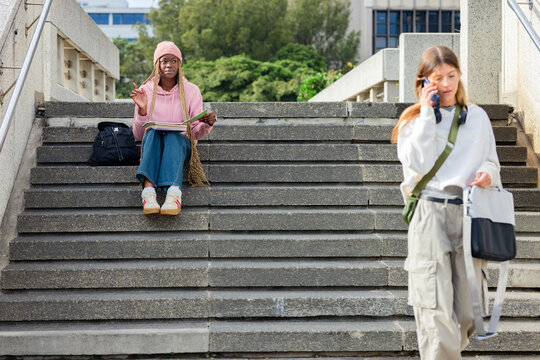 African American woman wearing pink hoodie on campus steps reviewing notebook with pen, copy space