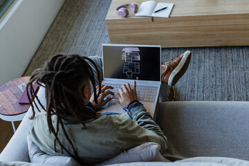 Laptop is displaying schematic plan on gray sofa near window beside pastel headphones