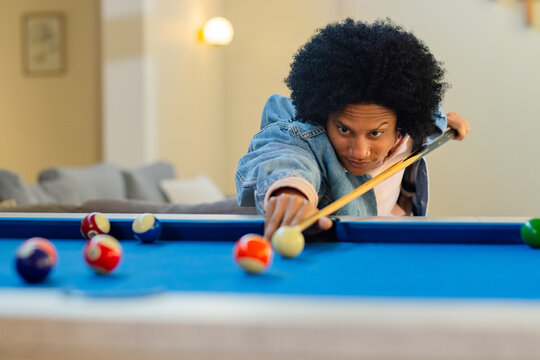 African American man leaning over blue pool table, aiming cue at cue ball in recreation room