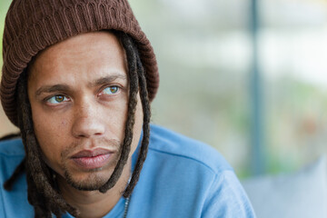 Man with dreadlocks gazing to right in lounge wearing brown beanie and blue top, copy space