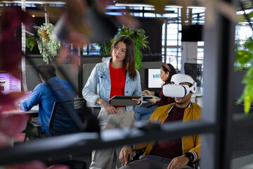 Diverse coworkers presenting virtual reality project in open-plan office using tablet and computers