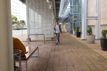 Asian man walking along brick walkway wearing plaid shirt and headphones holding smartphone