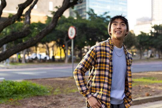 Asian man standing on park road with beanie, chain necklace beside no parking sign, copy space