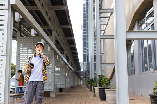 Male holding paper cup and checking smartphone on walkway, Asian male passing folder, copy space