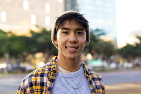 Asian man standing in park by street in afternoon with beige beanie and silver chain necklace