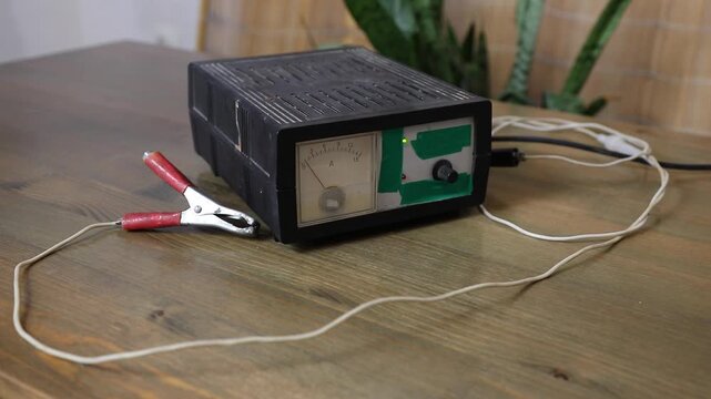 Manual battery charger with voltmeter showing power indicators on a wooden table. Automotive repair and maintenance concept.