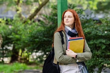Teenage student holding colorful notebooks, wearing smartwatch and backpack on campus path