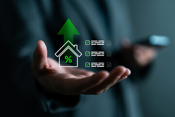 Close-up of hand with digital overlay of house, percentage symbol, checklist and upward arrow. Represents rising property value, real estate investment, mortgage rates or home loans.