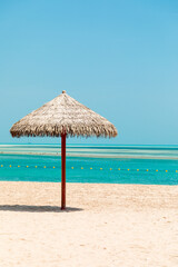 Beach scene with straw thatched umbrella over sandy shore and turquoise waters for vacation and travel images