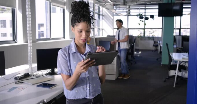 Diverse coworkers tapping tablet and discussing project under daylight in open-plan office