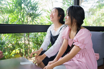 Two teenage girls laughing together inside a café, enjoying a relaxed moment with natural light and greenery, expressing friendship, joy, and casual lifestyle.