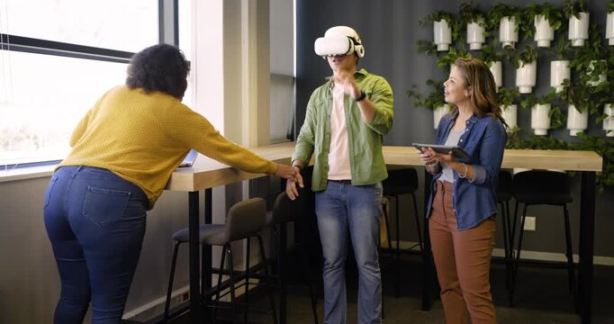 Diverse coworkers typing on laptop guiding headset user with tablet navigating, nodding at office