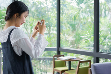 Fototapeta premium Teenage girl standing and taking a photo with her smartphone inside a café, expressing creativity, focus, and modern digital lifestyle in a bright natural environment