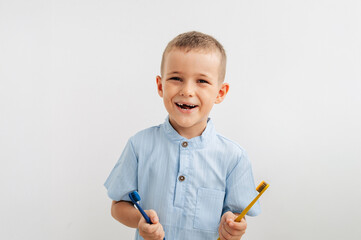 child holding yellow and blue toothbrushes, smiling with a missing baby tooth
