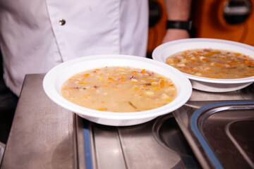 Chef serving hearty vegetable soup in white bowls at kitchen counter