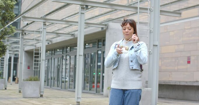 Mid adult woman holding take-out bowl under pergola inspecting contents before taking next bite