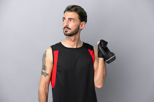 Young caucasian man isolated on grey background making weightlifting with kettlebell - Powered by Adobe