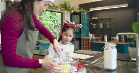 Mother and Asian Indian daughter cracking egg into bowl, whisking baking batter at kitchen island - Powered by Adobe