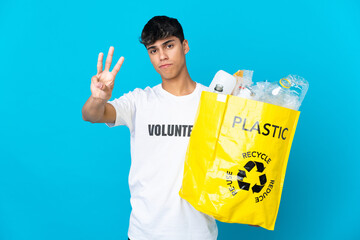 holding a bag full of plastic bottles to recycle over blue background happy and counting three with fingers