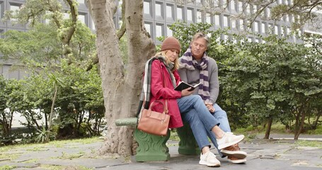 Senior couple entering garden and sitting on green bench while reading book for shared enjoyment