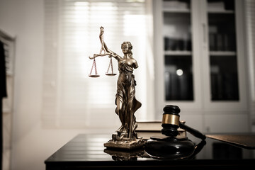 A bronze-toned Lady Justice statue stands centered beside courtroom gavel on polished desk,...