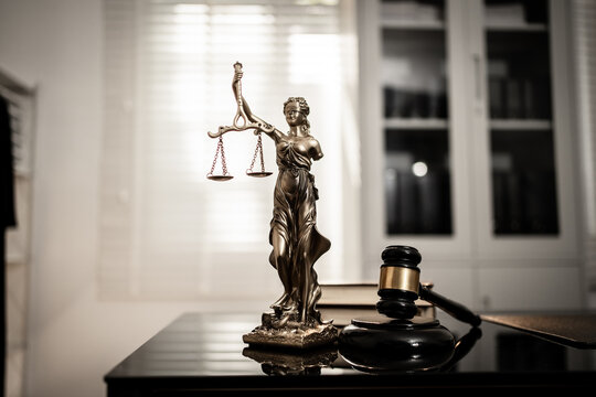 A bronze-toned Lady Justice statue stands centered beside courtroom gavel on polished desk, reflecting soft light against blurred legal-office, fairness, digital law, modern judicial integrity.