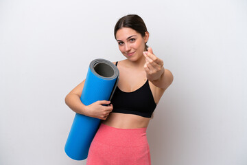 Young sport girl going to yoga classes while holding a mat isolated on white background making money gesture