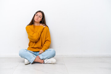 Young girl sitting on the floor isolated on white background suffering from pain in shoulder for having made an effort