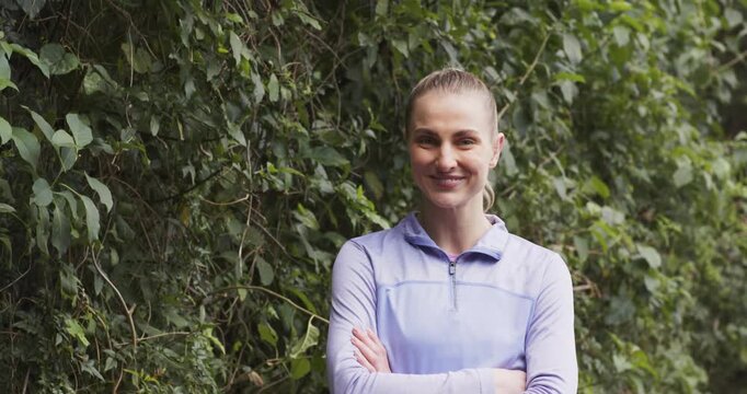 Woman in purple top crossing arms on garden path shifting from smirk to laugh reacting offcamera