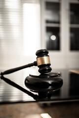 A polished wooden gavel resting on a glossy black surface illuminated by soft directional light, symbolizing justice, legal authority, courtroom decisions, professional