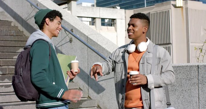 Diverse male students greeting with high-five catching up while sipping coffee on campus stairs
