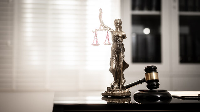 A bronze-toned Lady Justice statue stands centered beside courtroom gavel on polished desk, reflecting soft light against blurred legal-office, fairness, digital law, modern judicial integrity.