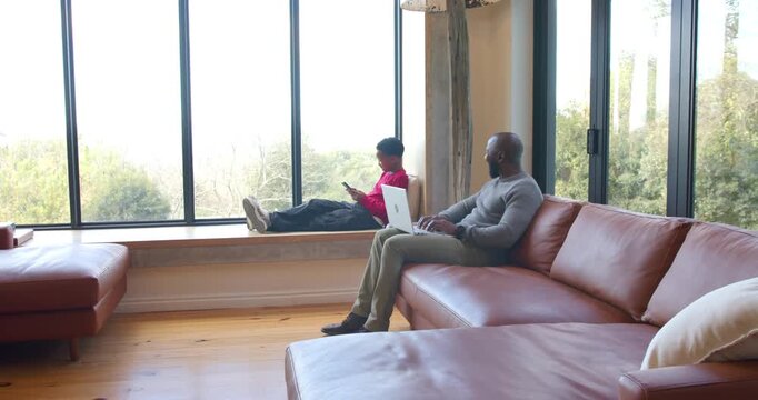 African American father and son at home, father starting work on laptop while son scrolling phone