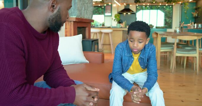 African American father clapping and encouraging anxious son fidgeting on sofa in living room