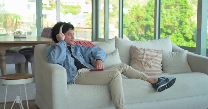 Man tapping smartphone then donning wireless headphones on sofa by glass doors for audio listening